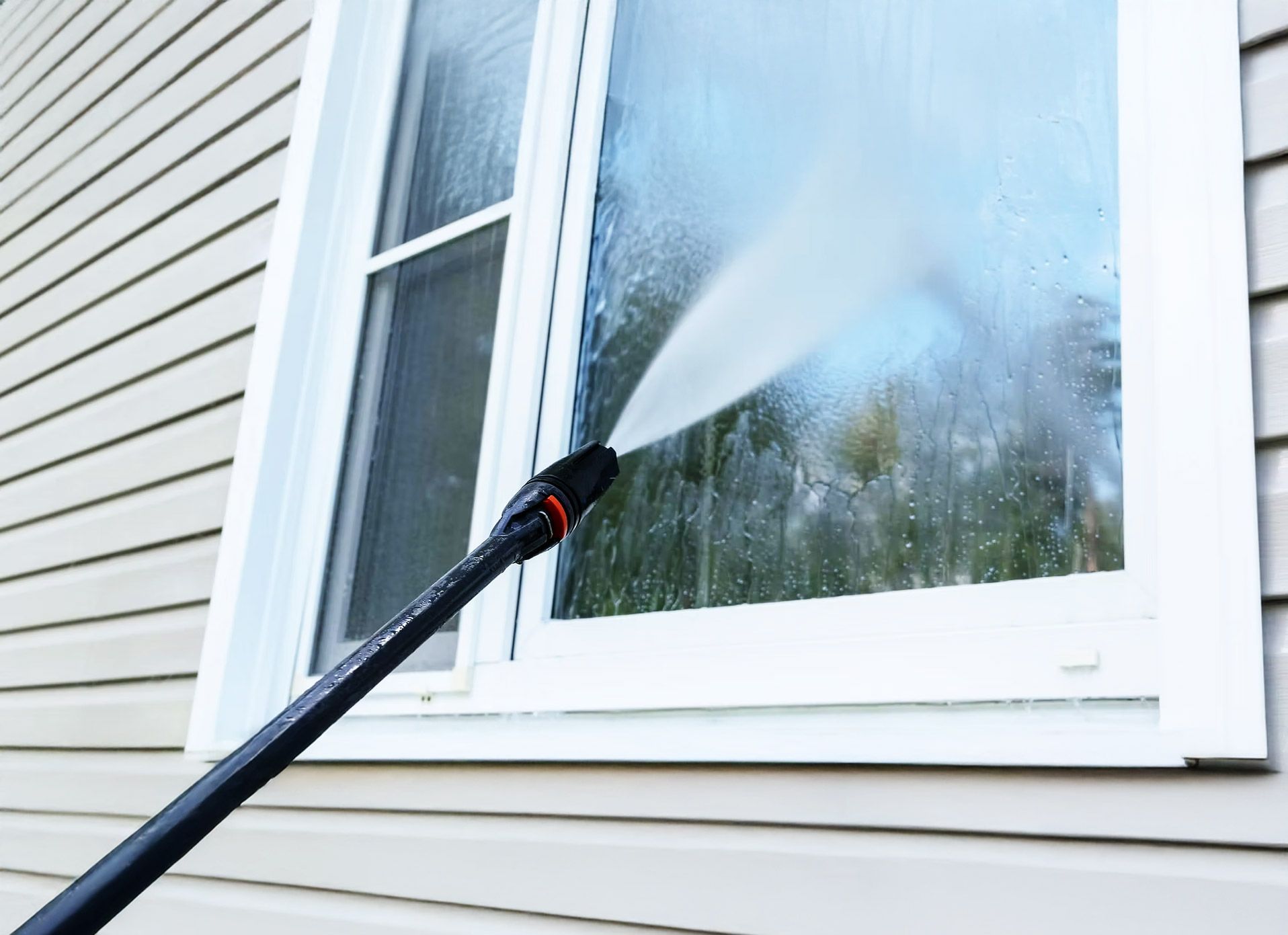 Pressure washer spraying water onto a window of a house.
