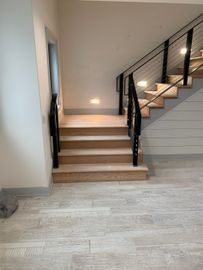 Staircase with wooden steps and black railing. Built-in lights illuminate the stairs and surrounding wall.