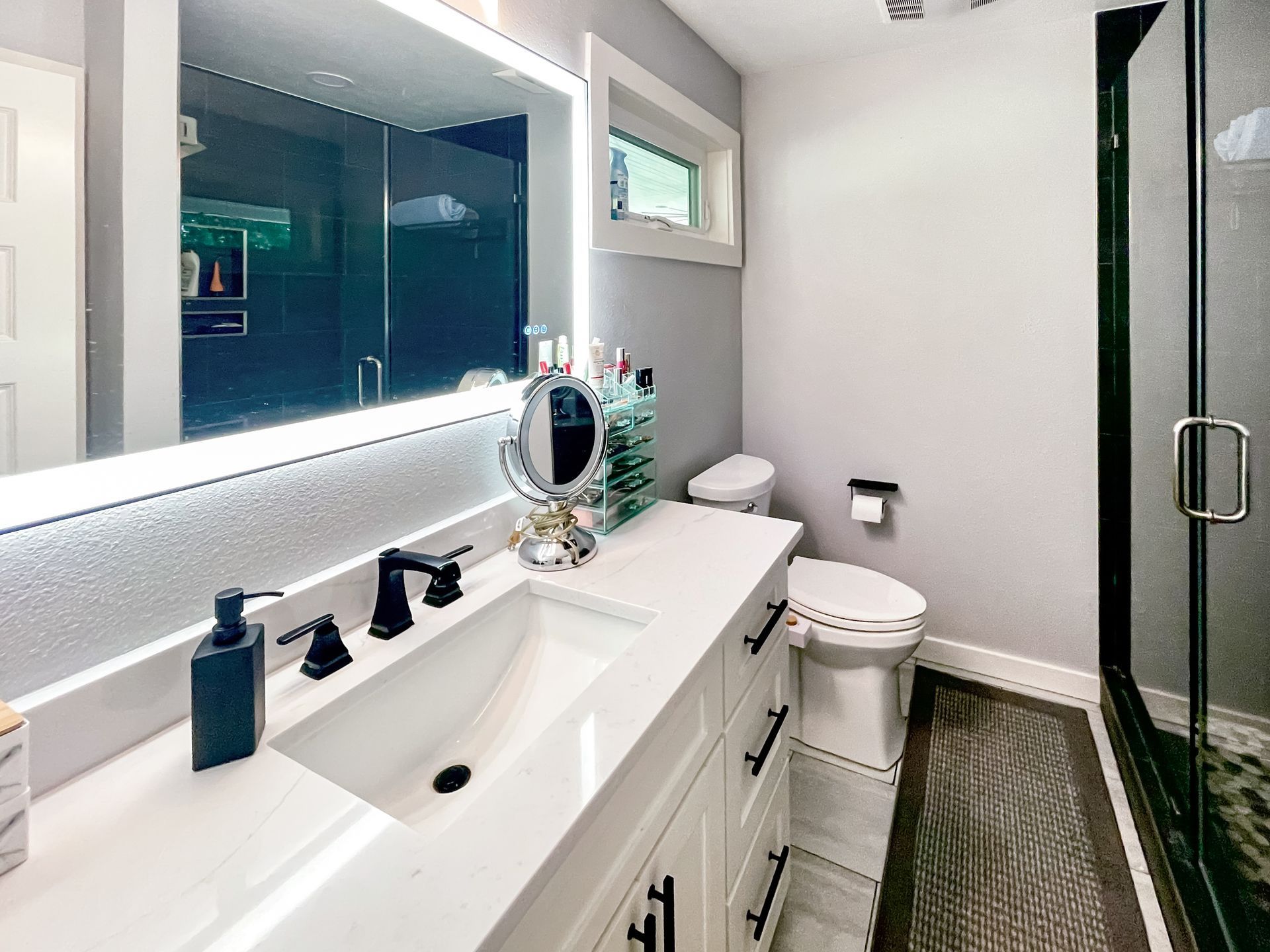 Modern bathroom with white vanity, black faucet, and lighted mirror. Shower with glass door.
