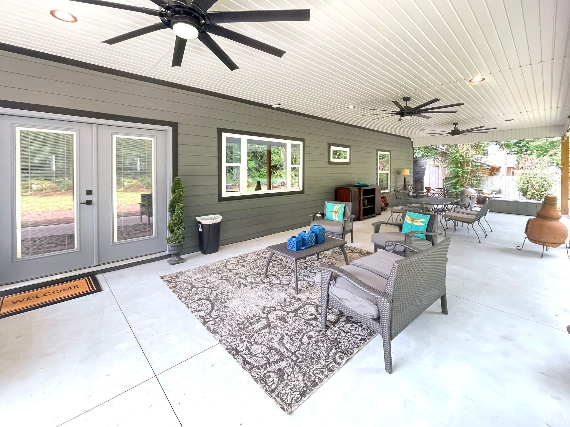 Covered outdoor patio with seating, rug, and a gray door.