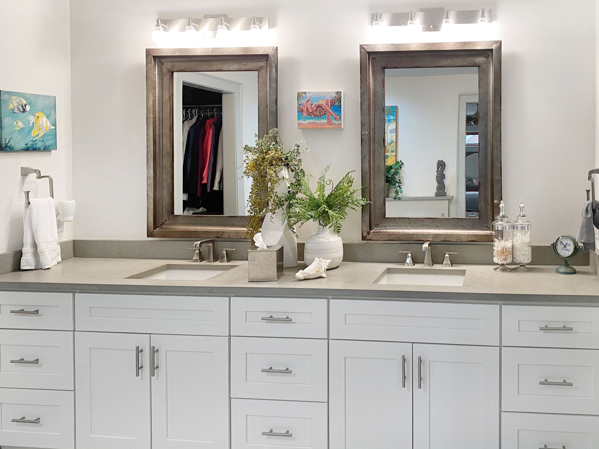 Double bathroom vanity with white cabinets, gray countertop, wood-framed mirrors, and floral arrangement.