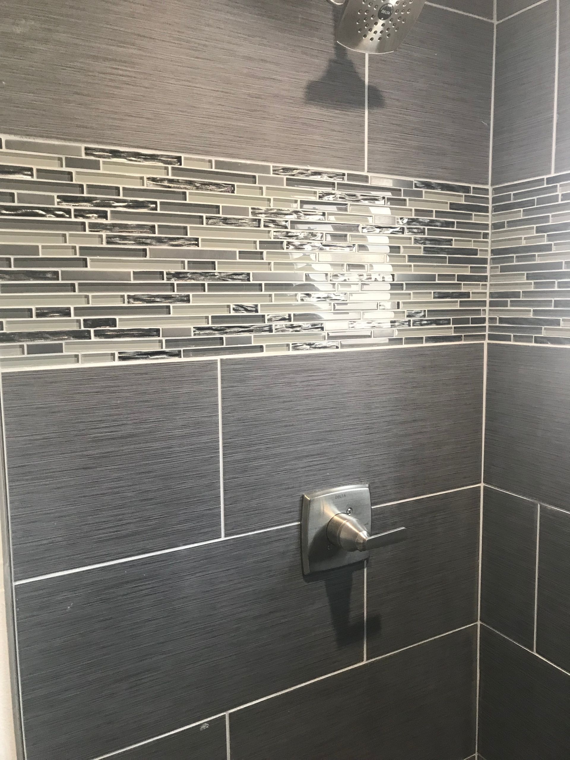 Dark tiled shower with decorative mosaic tile border, shower head, and faucet.