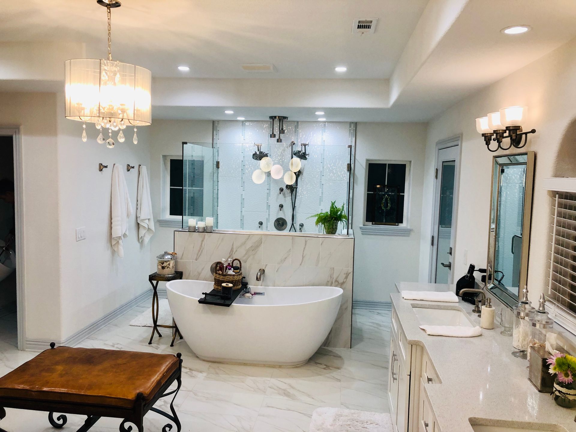 Luxurious white bathroom with soaking tub, marble accents, and chandelier lighting.