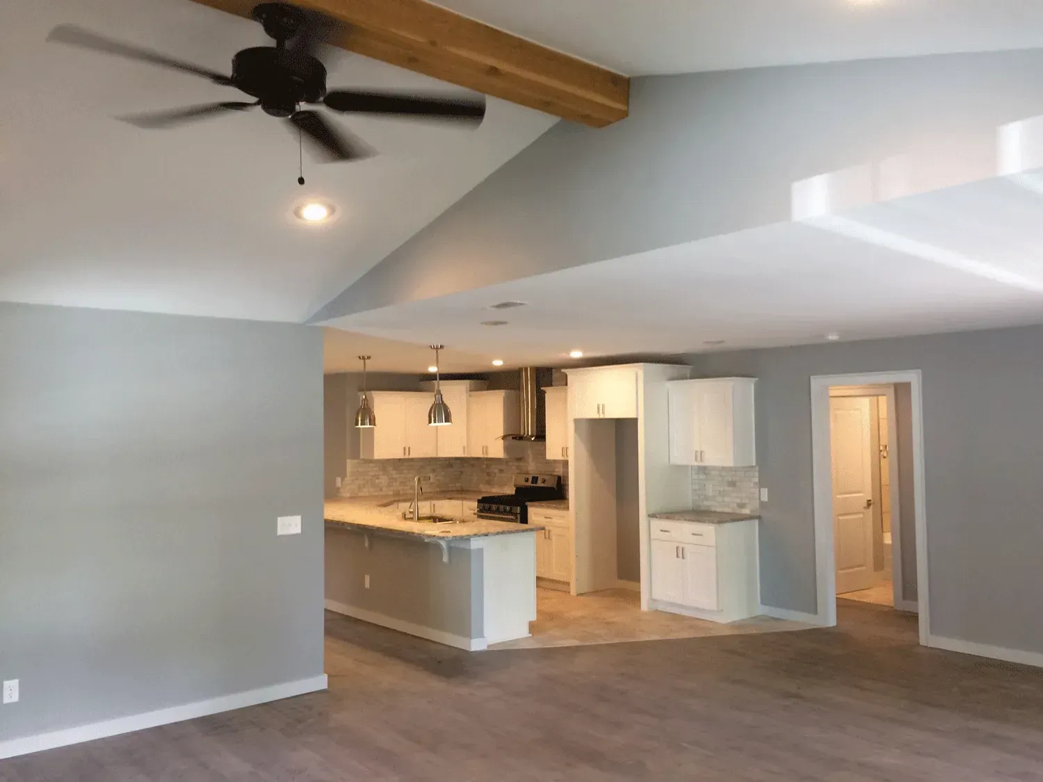 Spacious, open-concept living area with kitchen in the background, featuring high ceilings and a wooden beam.