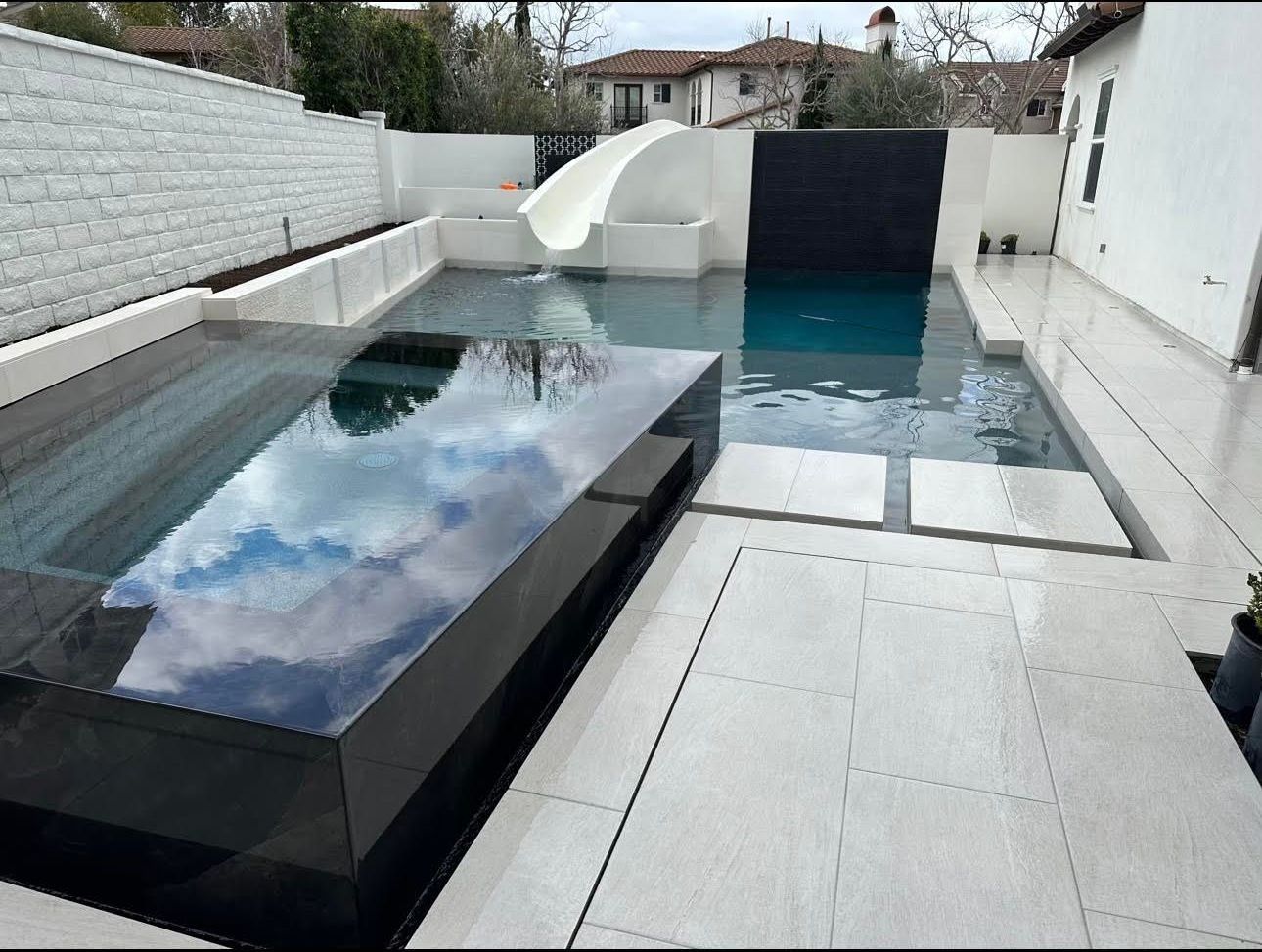 Modern backyard pool with a black rectangular jacuzzi, slide, and waterfall feature.