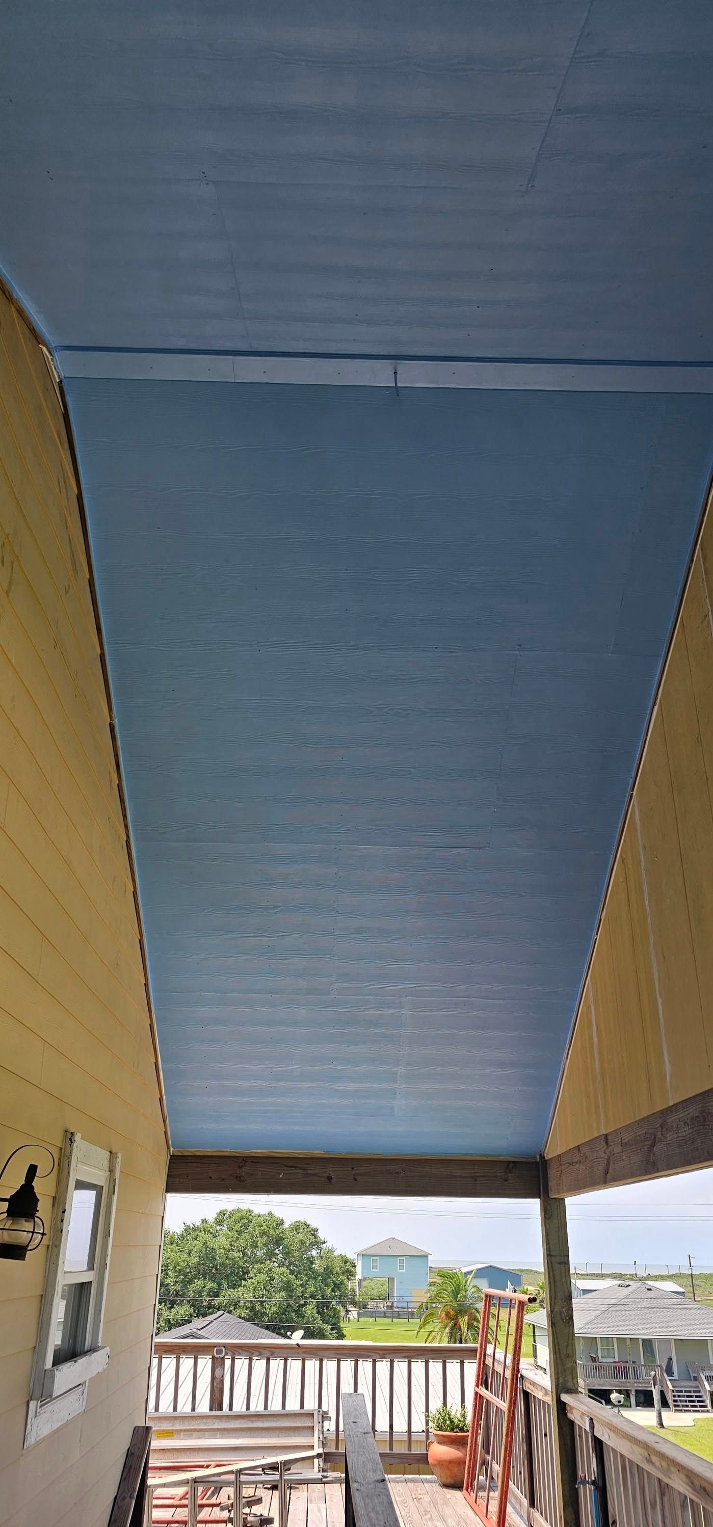 View from a balcony looking out at a blue-painted ceiling, wooden railings, and surrounding neighborhood houses.
