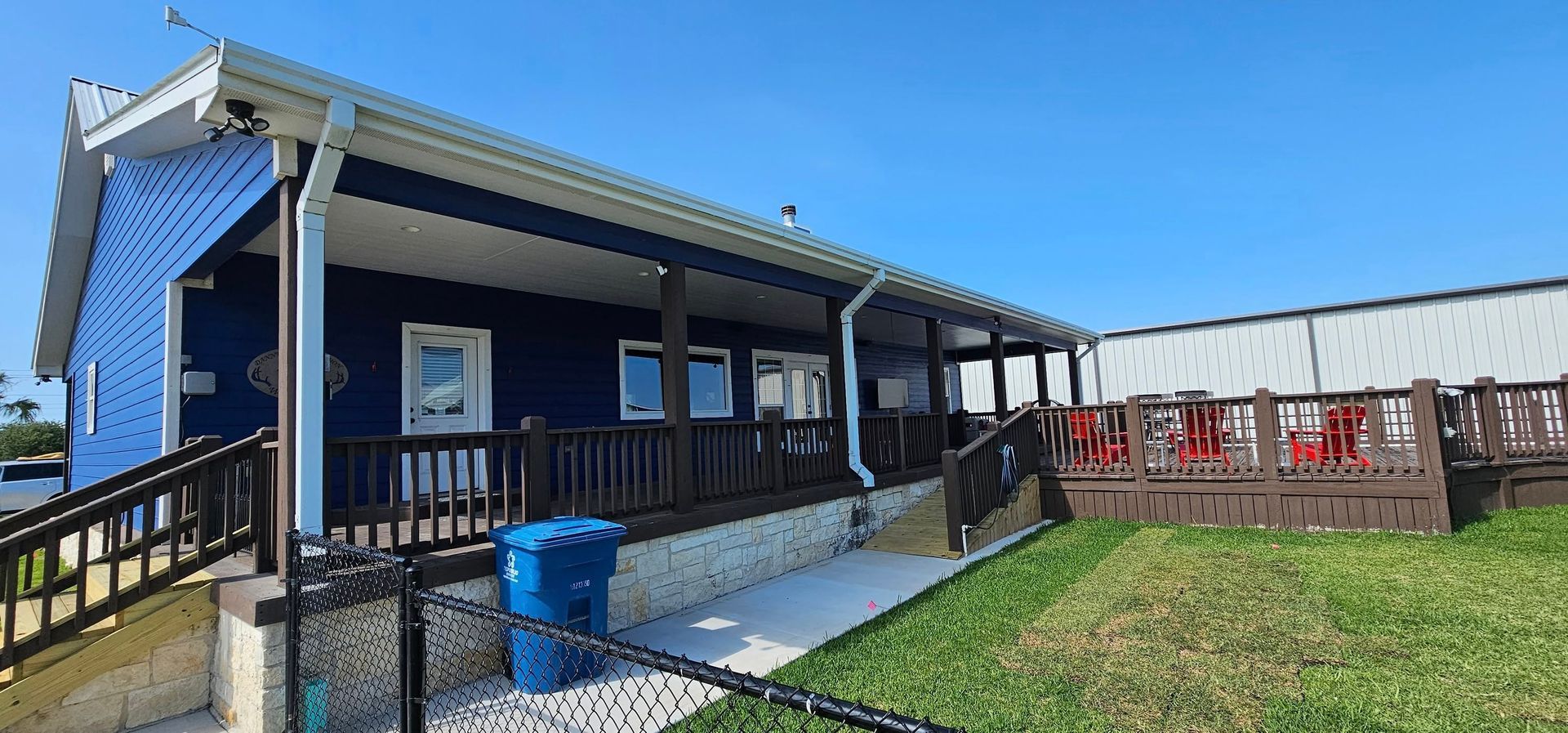 A blue building with a covered deck, ramp, and stairs, set against a clear blue sky on a sunny day.