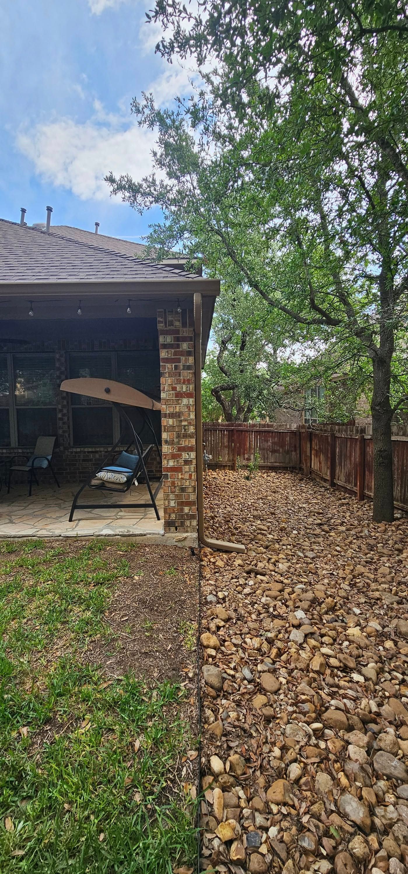 A backyard patio with a brick corner column, a lawn, and a large area covered in river rocks near a wooden fence.
