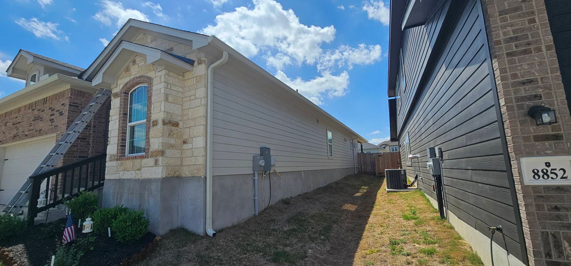 A side view showing the narrow space between two residential houses with tan stone and beige siding and grey panels.