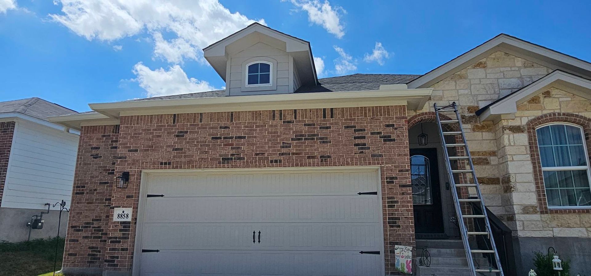 A house with a brick garage facade and a dormer window, featuring a metal ladder leaning against the stone entrance.