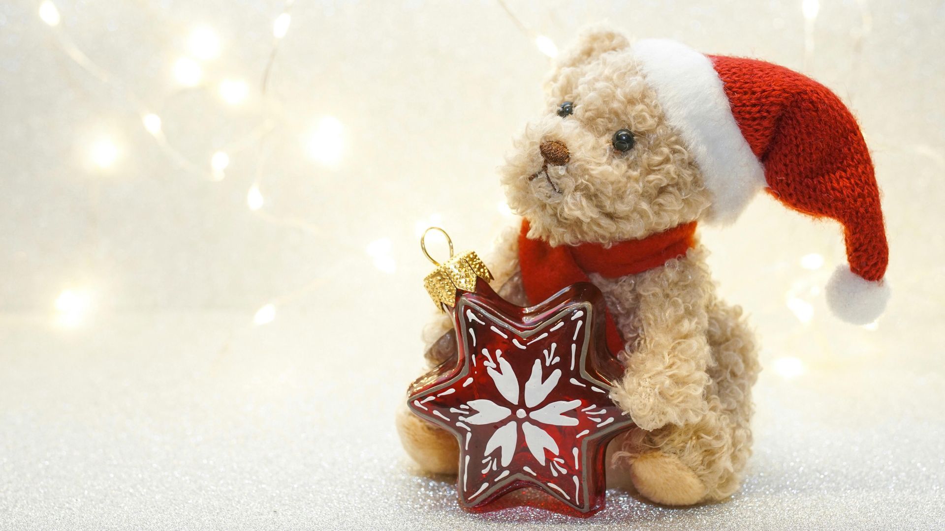 A teddy bear wearing a santa hat and scarf is holding a christmas star.