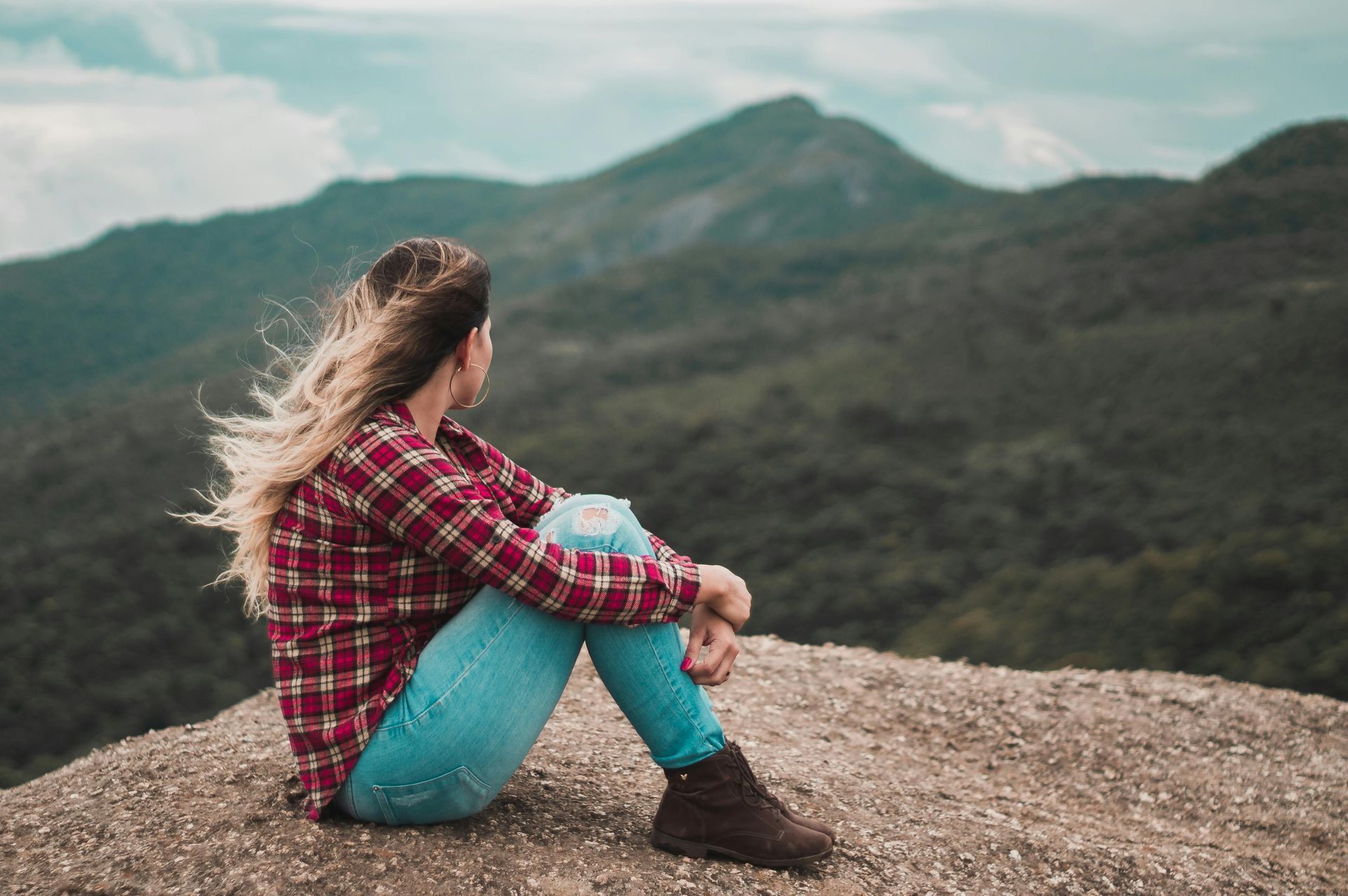 A woman is sitting on top of a rock looking at the mountains.