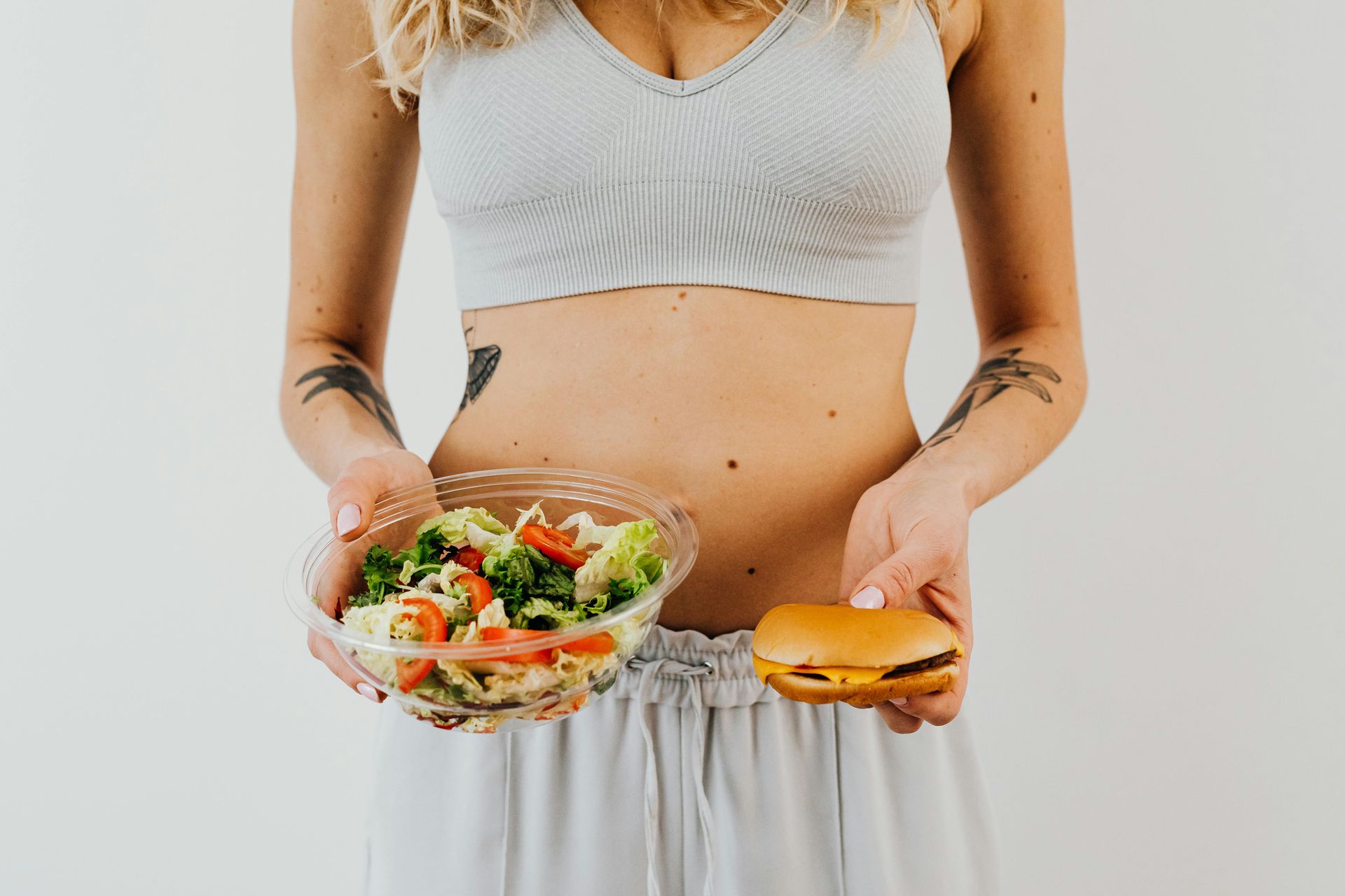 A woman is holding a bowl of salad and a hamburger.