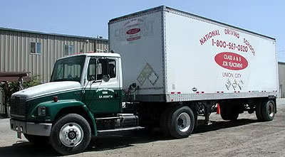 Green box truck with white cargo trailer parked outside a warehouse