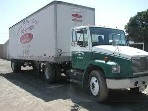 Green and white box truck parked outdoors on a sunny day