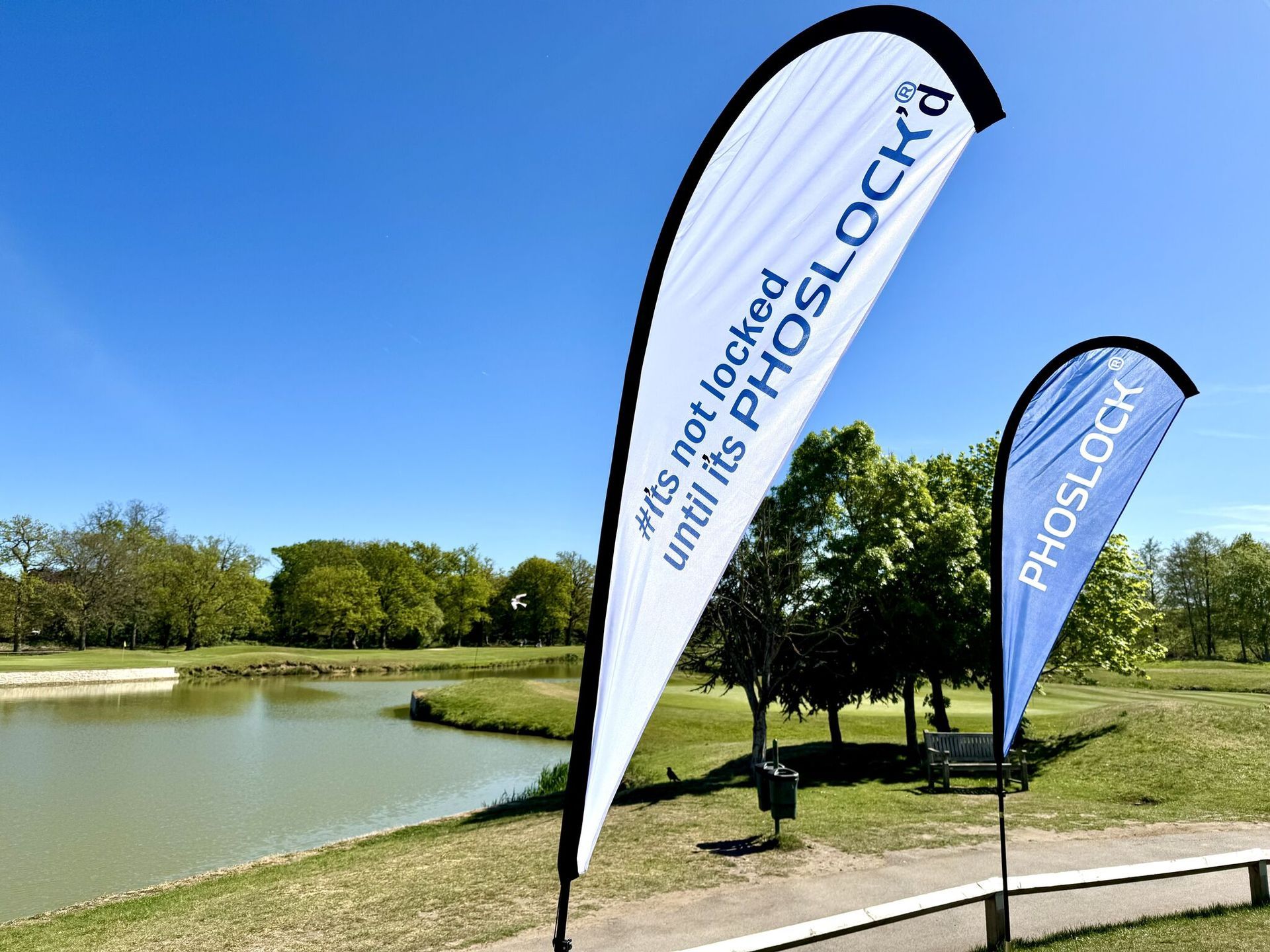 Blue PHOSLOCK flags by a pond in a sunny park.
