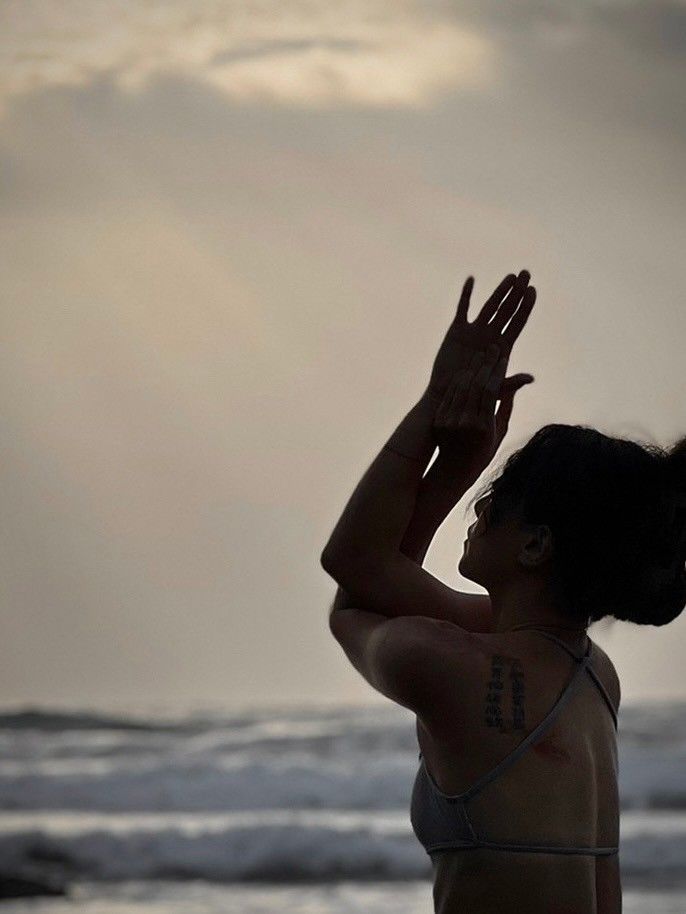 A woman in a bikini is standing on the beach with her arms outstretched.