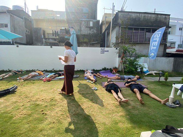 A woman is standing next to a group of people laying on the grass.