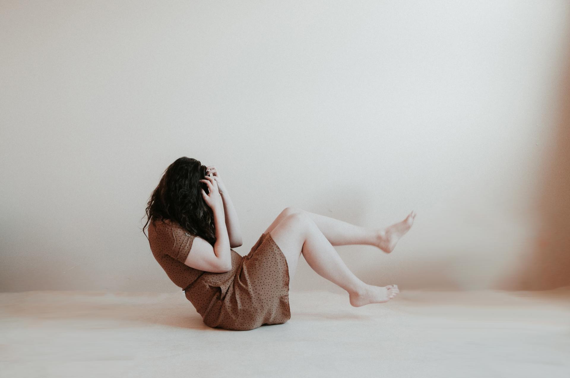 A woman in a brown dress is sitting on the floor with her legs crossed.