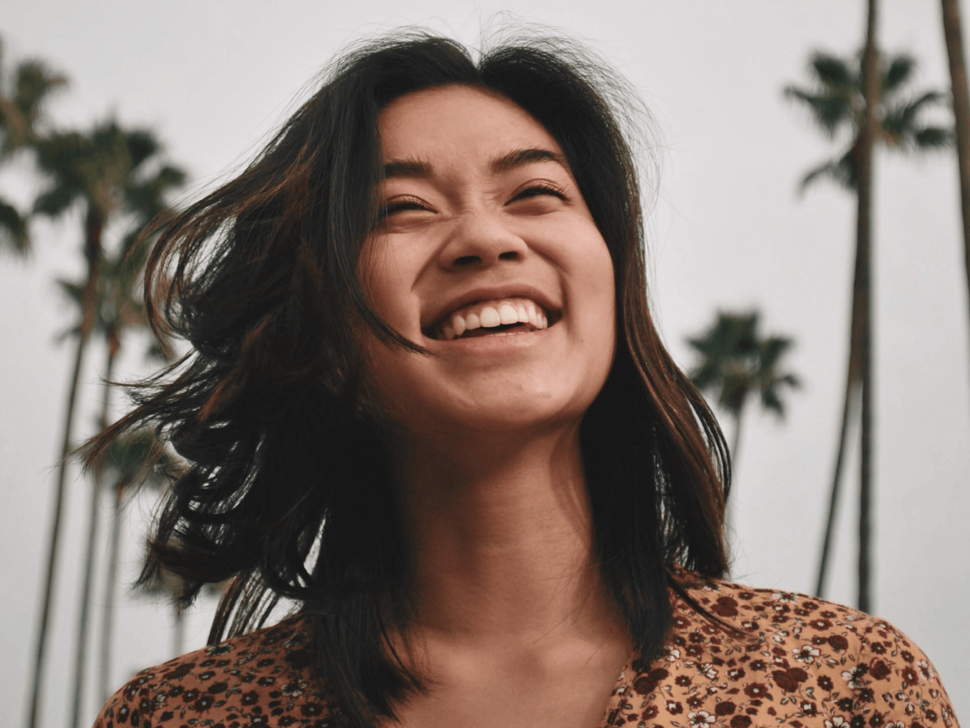 A woman is smiling with palm trees in the background.