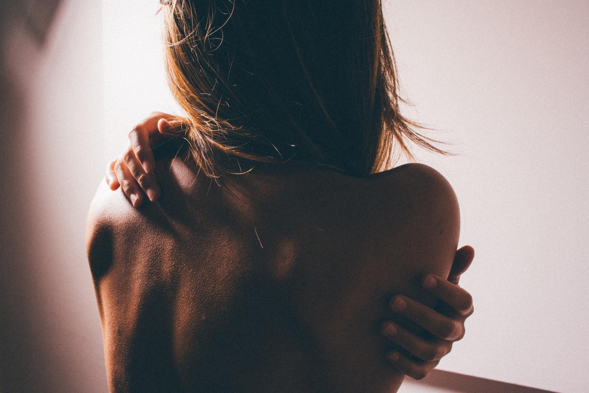 A woman is holding her shoulder in pain while standing in front of a wall.