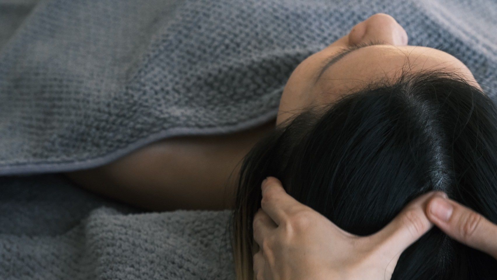 A woman is laying on a bed getting a head massage.
