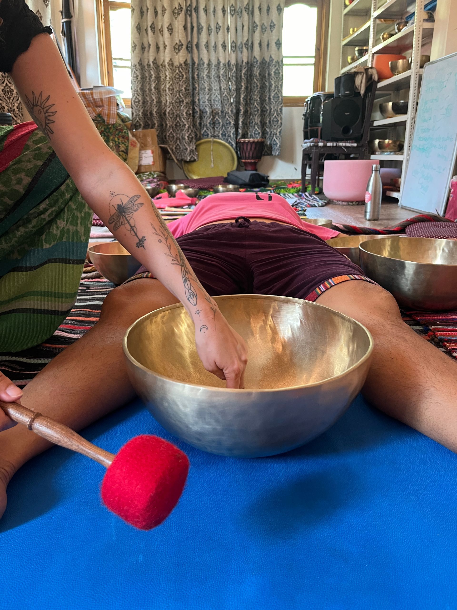 A person is laying on the floor playing a bowl with a stick.