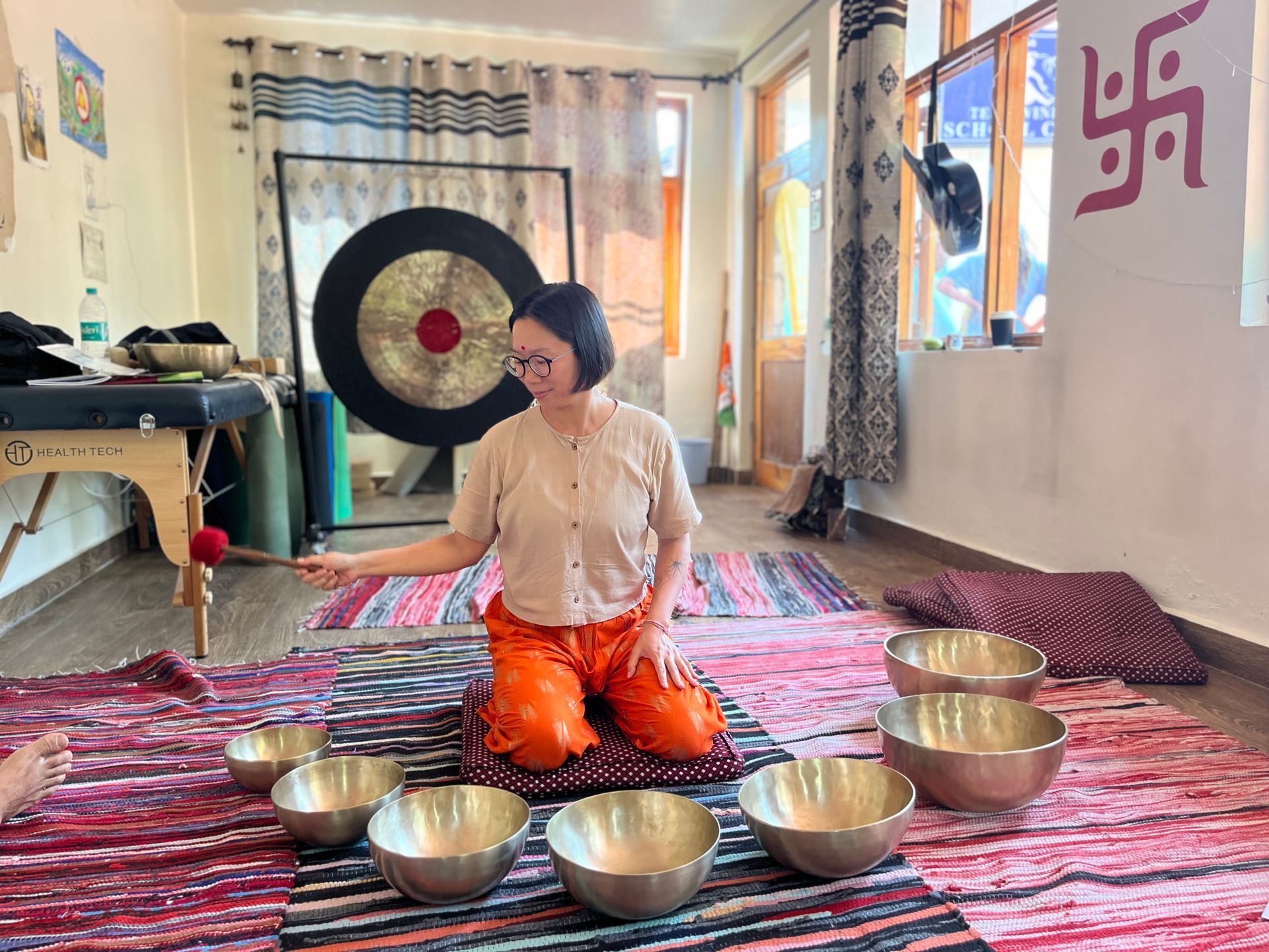 A woman is kneeling down in front of a gong and bowls in a room.