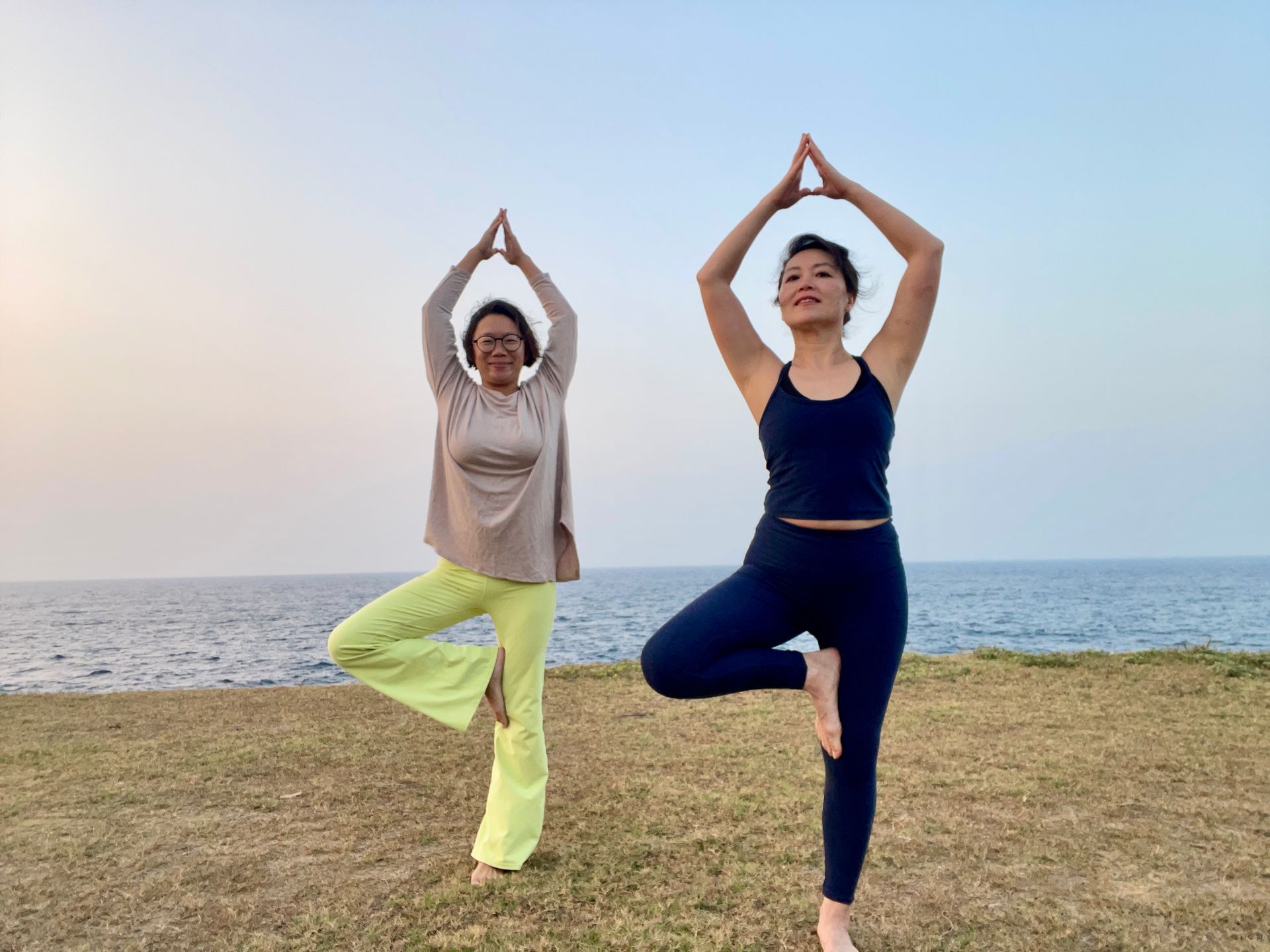 Two women are doing yoga on the beach near the ocean.