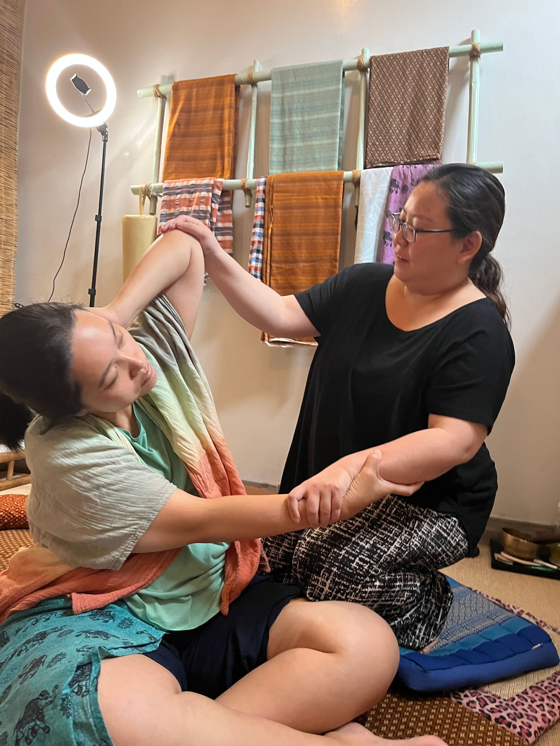 A woman is stretching another woman 's arm in a room.