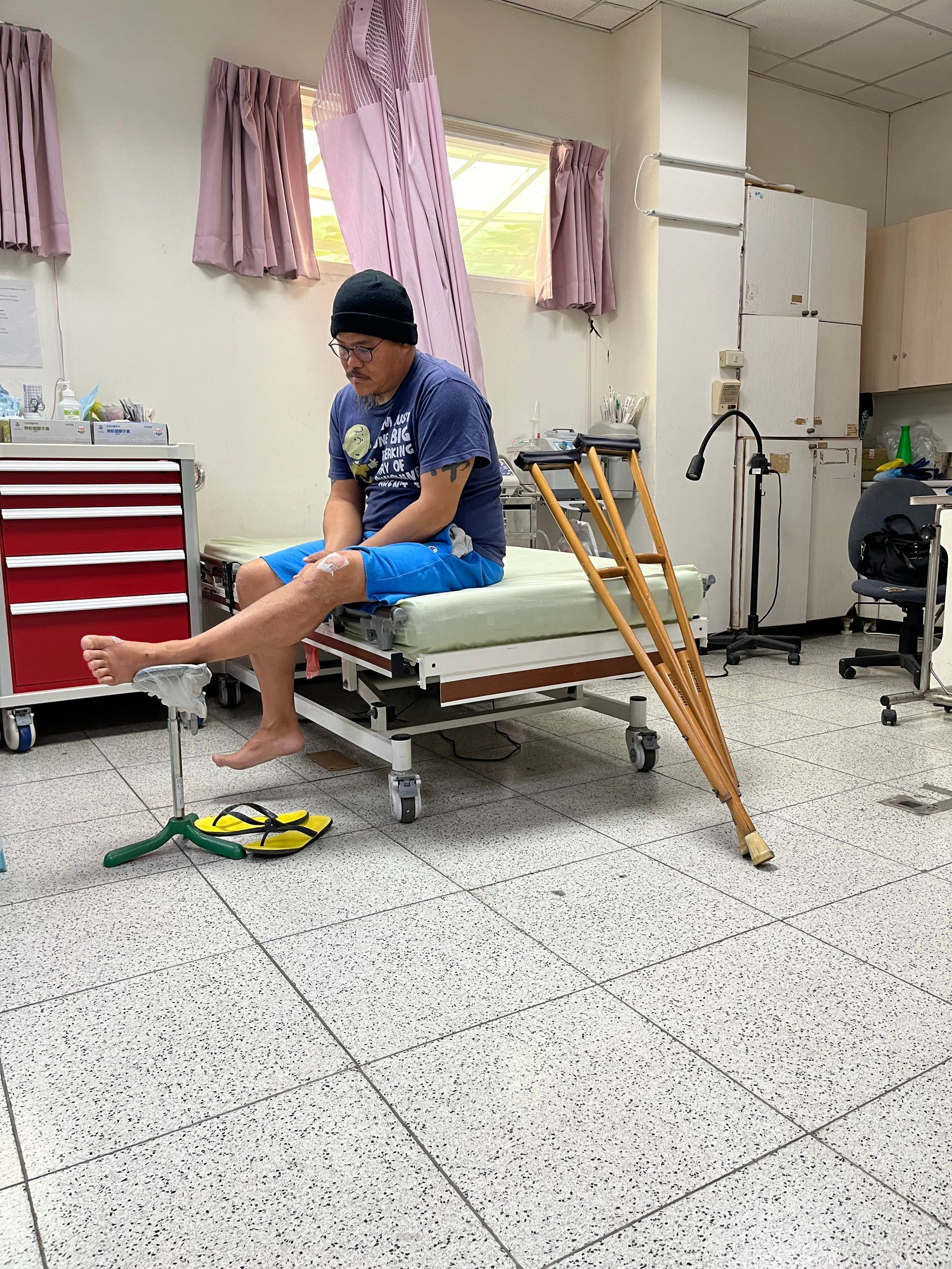 A man is sitting on a hospital bed with crutches.