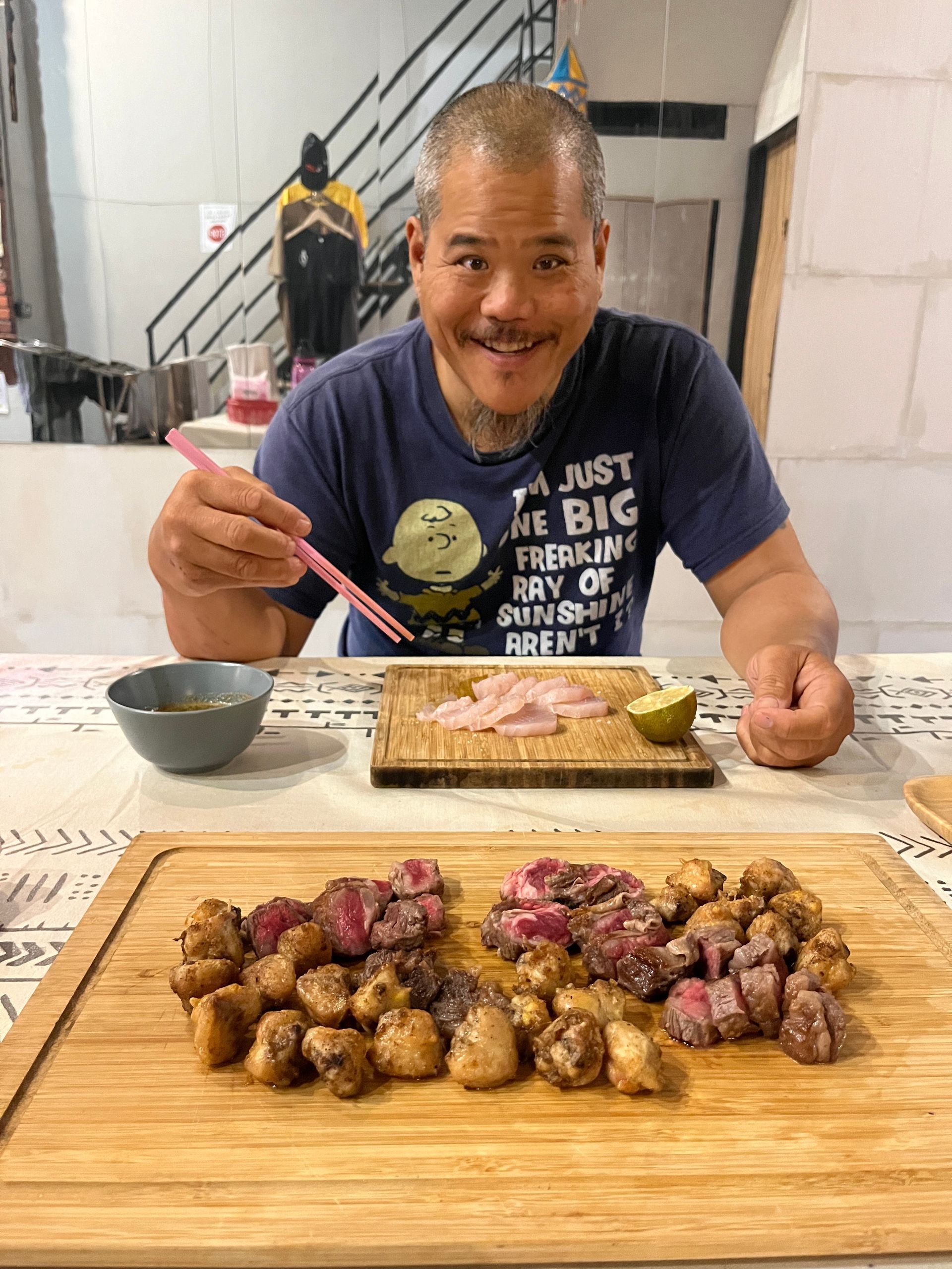 A man is sitting at a table eating food with chopsticks.
