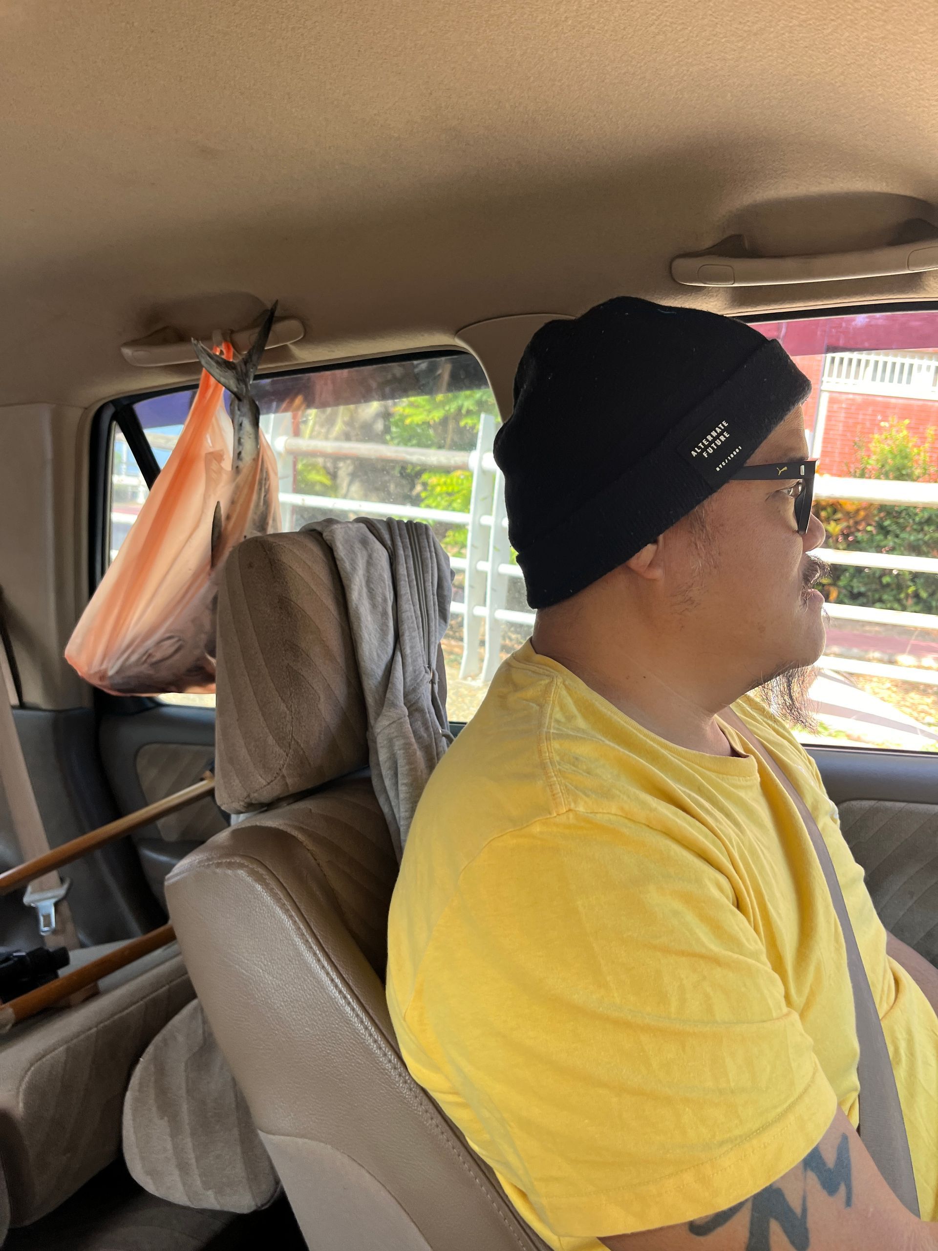 A man in a yellow shirt and black hat is sitting in the back seat of a car.