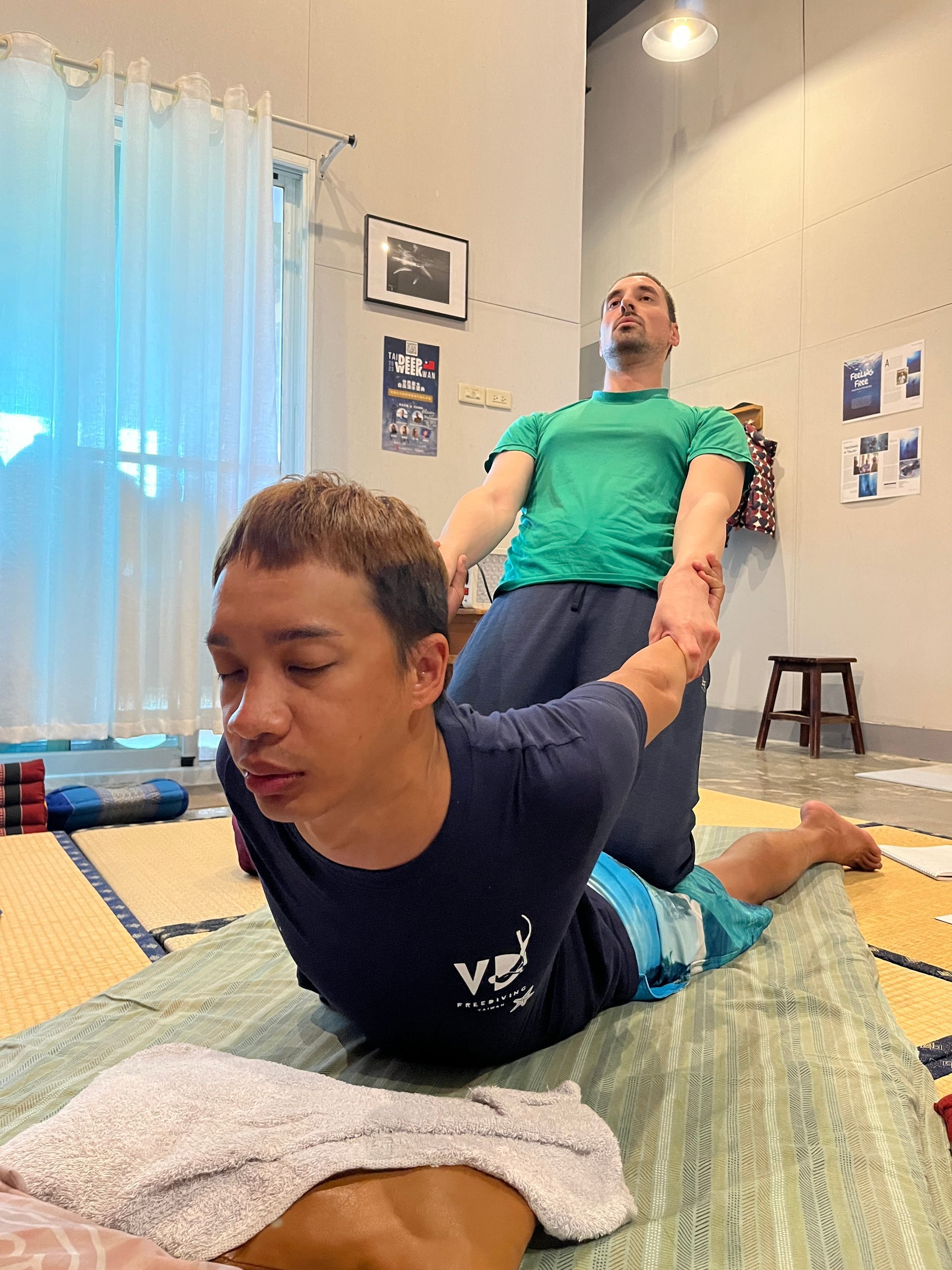 A man is laying on the floor getting a massage from another man.