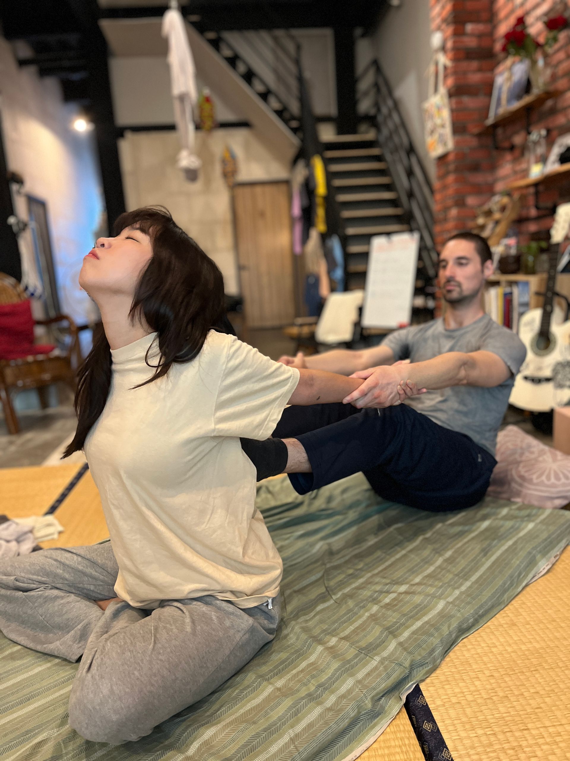 A man and a woman are sitting on a bed stretching their legs.