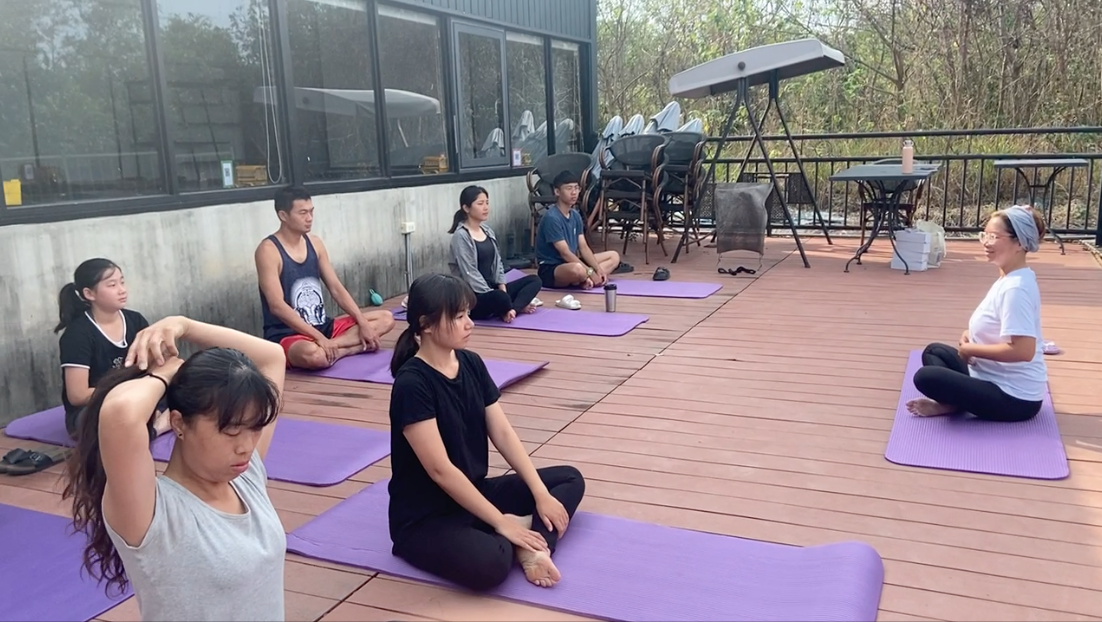 A group of people are sitting on yoga mats on a patio.