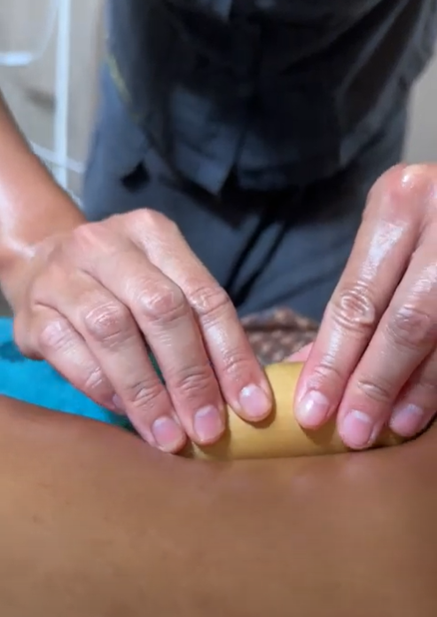 A person is giving a massage to another person with a bamboo stick.
