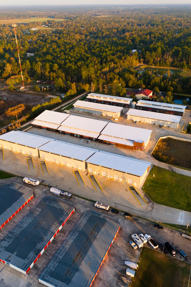 Aerial view of storage units and buildings with a forest backdrop.