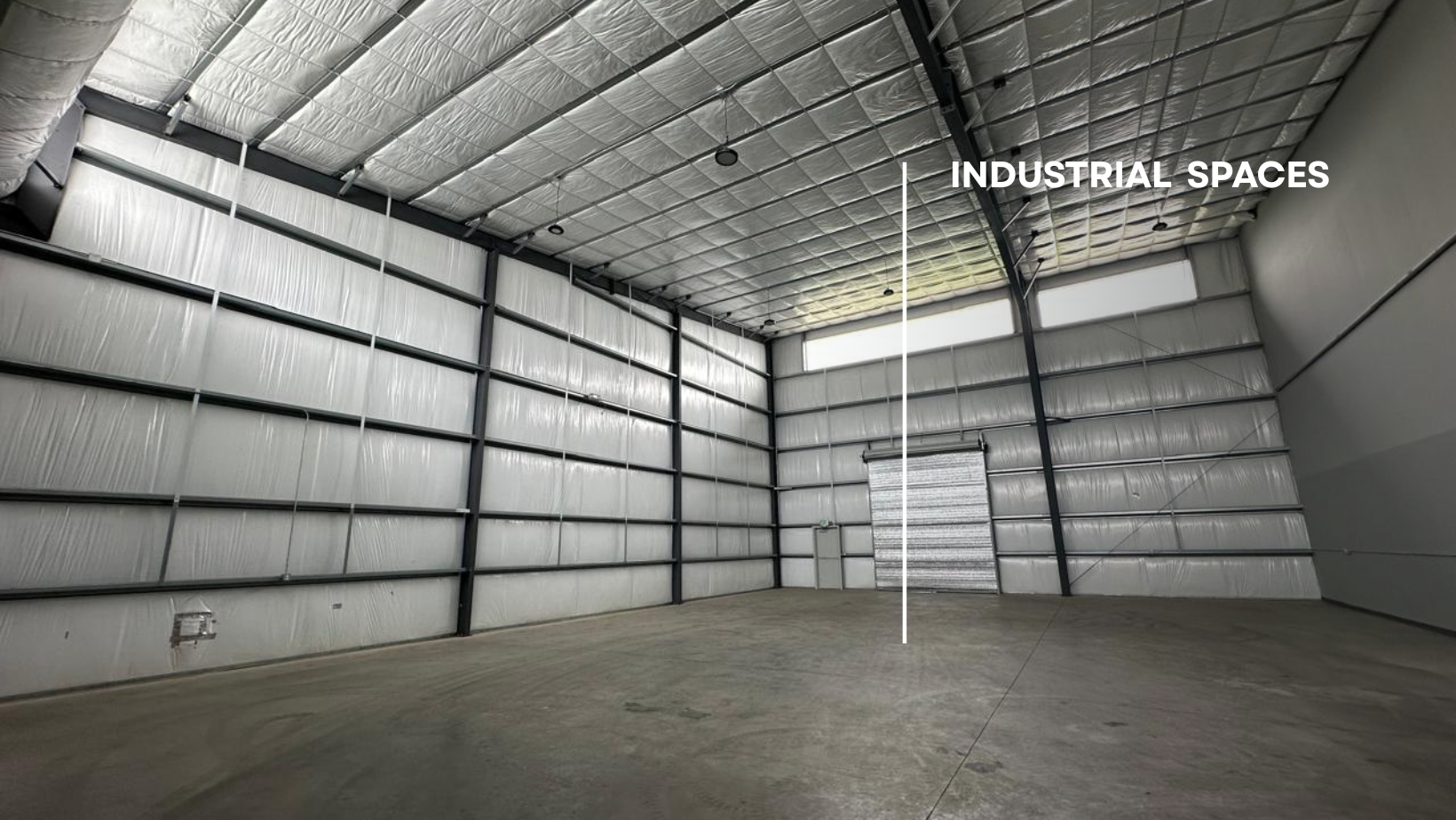 Empty industrial warehouse interior with metal beams, insulated walls, and a roll-up door.