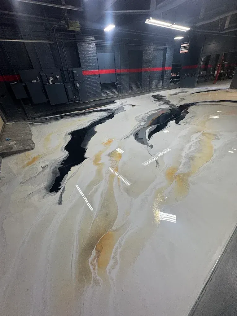 Large glossy epoxy floor with black, white, and gold marbling in a dim industrial space