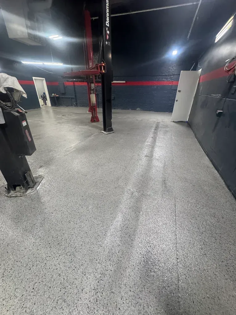Empty gym with speckled gray floor, black walls, red equipment, and overhead lights