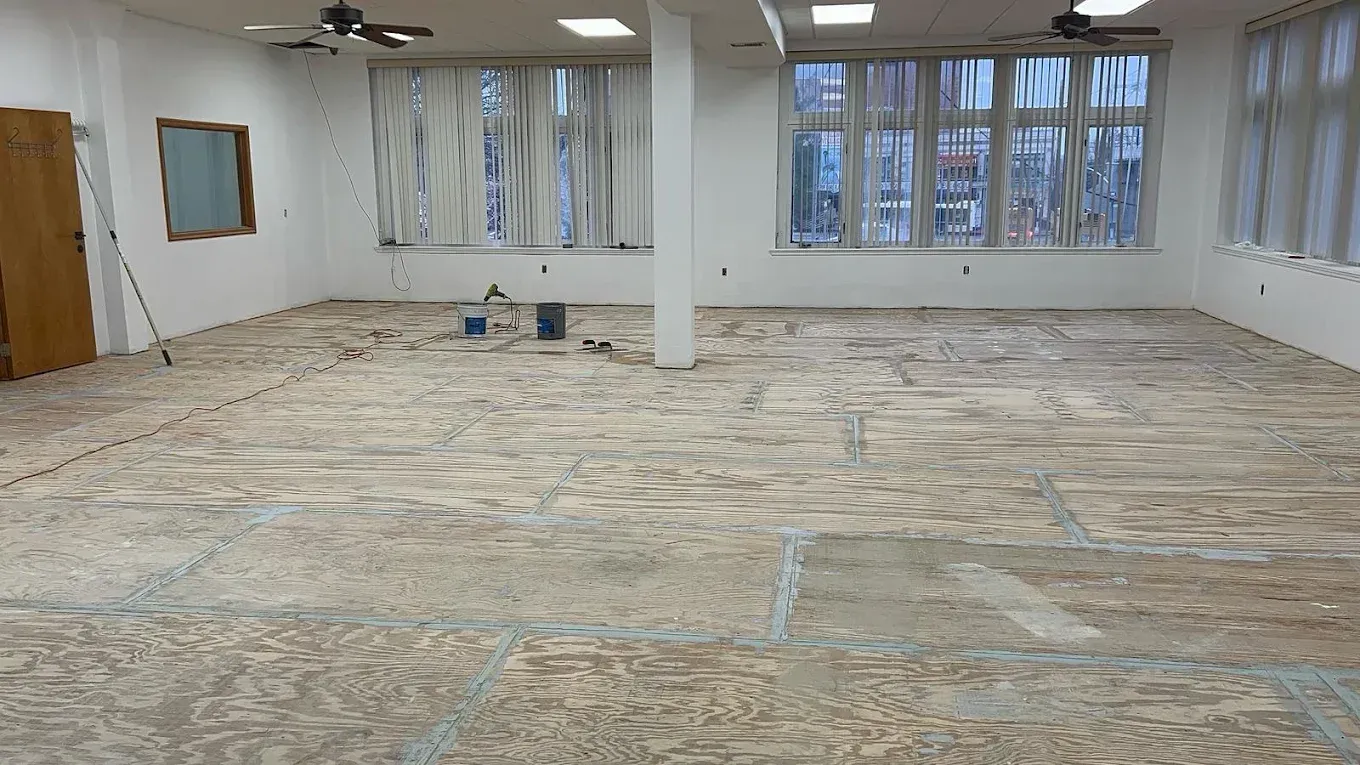 Empty room with bare subfloor, windows, white walls, and a central support column