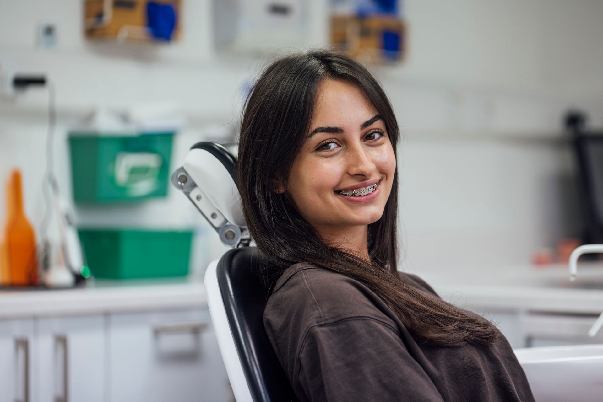A girl is smiling in a dentist's chair, showing her braces at Delgado Orthodontics, an expert on bra