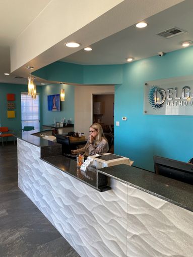 Reception area with textured white front desk, turquoise walls, and a person on the phone.