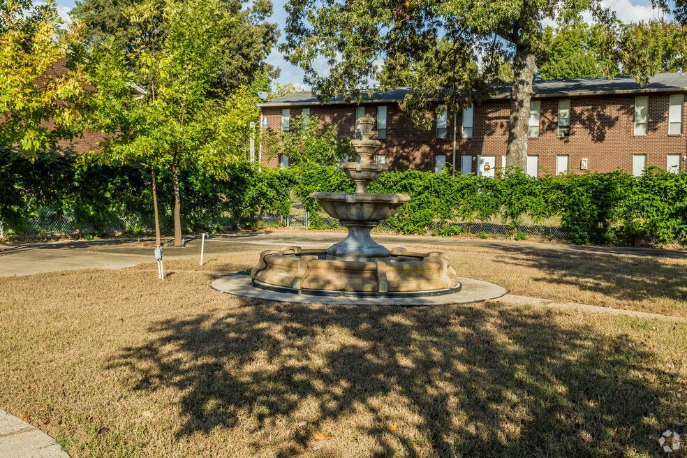 a fountain in a park with a brick building in the background