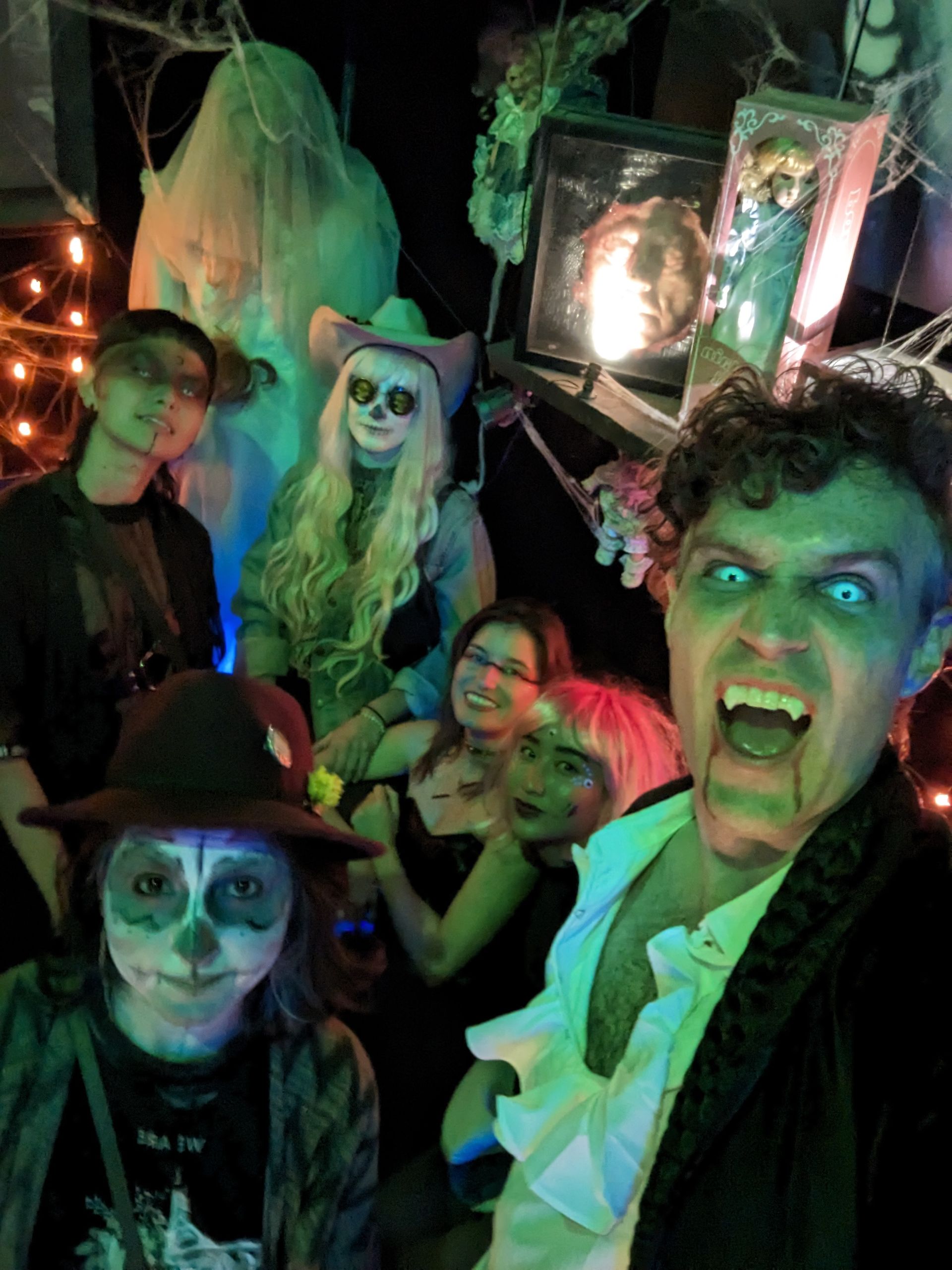 Group in Halloween costumes posing in front of spooky decorations, with a vampire in the foreground.