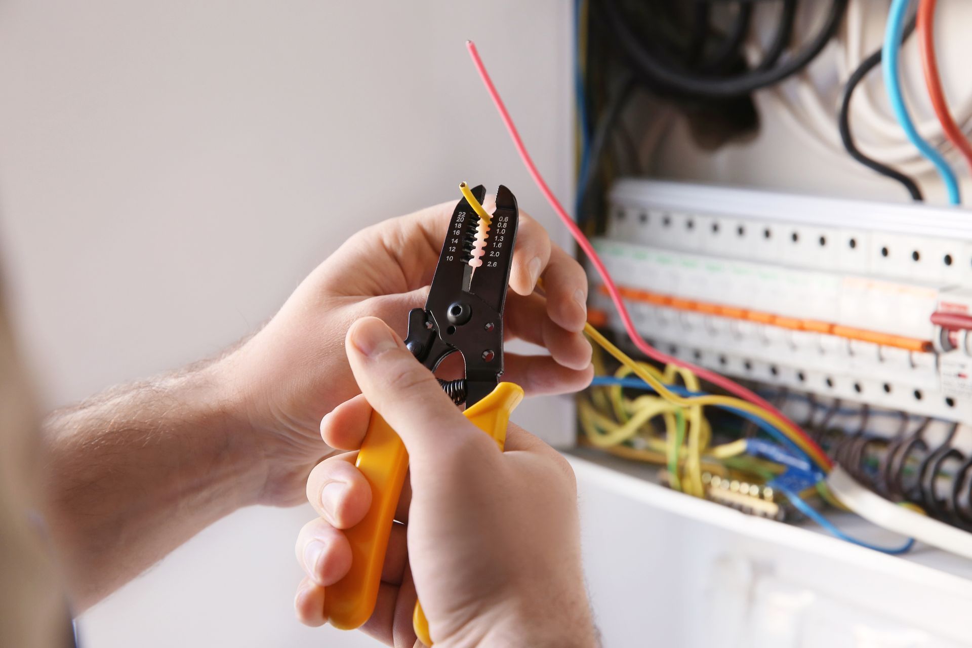 Hands using a wire stripper near a breadboard with connected colored wires in an electronics workspace