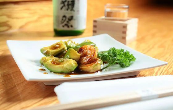 Plated glazed stuffed vegetables on a white dish with herbs, on a wooden table with chopsticks and a bottle behind