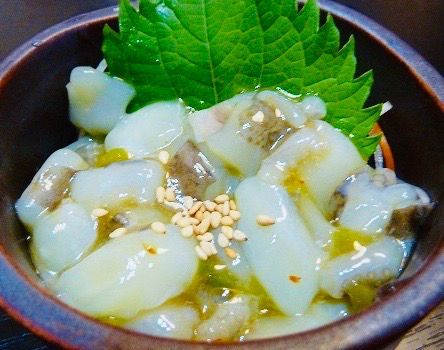 Small bowl of glossy white pickled vegetables topped with sesame seeds and a green leaf garnish