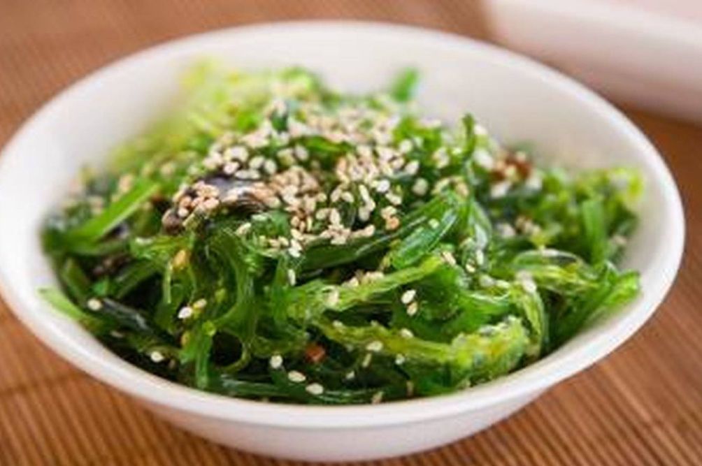 Bowl of green seaweed salad topped with sesame seeds on a wooden table